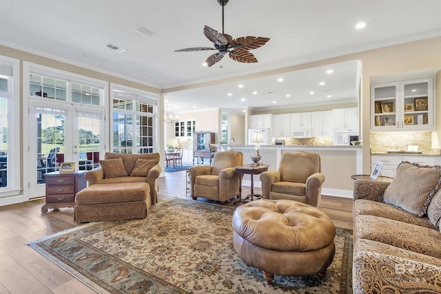 living room with crown molding, wood-type flooring, ceiling fan with notable chandelier, and french doors