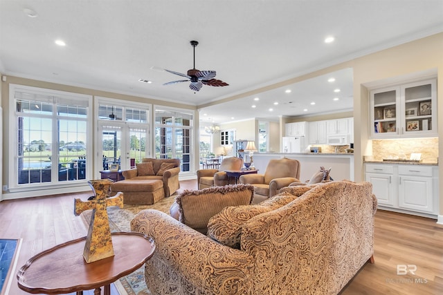 living room with crown molding, light hardwood / wood-style floors, ceiling fan with notable chandelier, and a healthy amount of sunlight