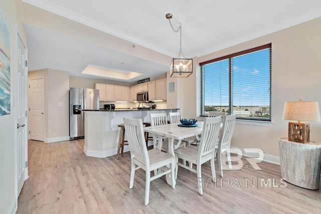 dining area featuring light hardwood / wood-style floors, a notable chandelier, ornamental molding, and a raised ceiling