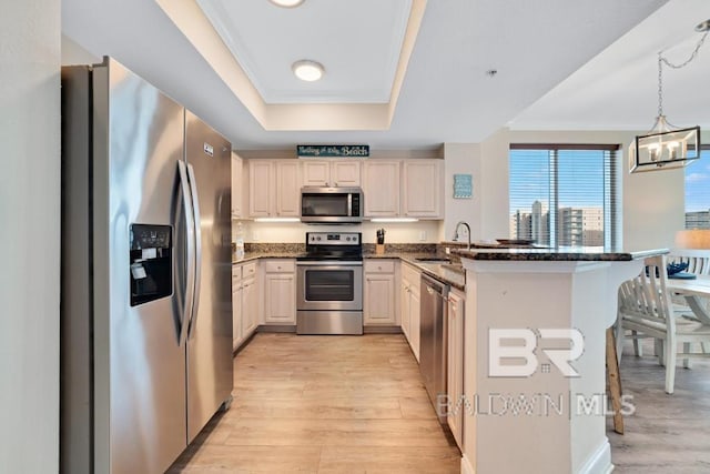 kitchen featuring appliances with stainless steel finishes, sink, kitchen peninsula, light hardwood / wood-style floors, and decorative light fixtures