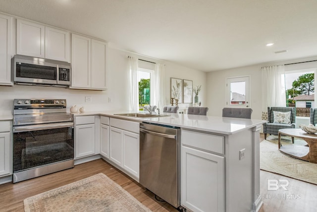 kitchen featuring a sink, appliances with stainless steel finishes, a peninsula, light wood finished floors, and light countertops