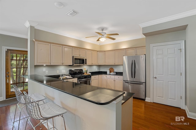 kitchen with dark wood-type flooring, stainless steel appliances, kitchen peninsula, a breakfast bar area, and ornamental molding