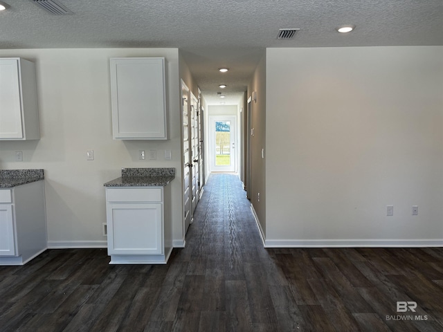 kitchen with dark stone counters, white cabinetry, dark wood-type flooring, and a textured ceiling