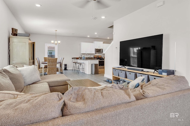 living room featuring ceiling fan with notable chandelier and light hardwood / wood-style flooring