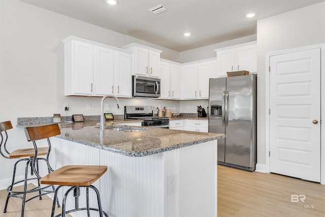 kitchen featuring kitchen peninsula, white cabinetry, dark stone counters, and appliances with stainless steel finishes