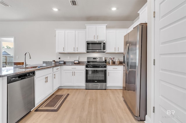 kitchen featuring appliances with stainless steel finishes, sink, dark stone countertops, white cabinets, and light hardwood / wood-style floors