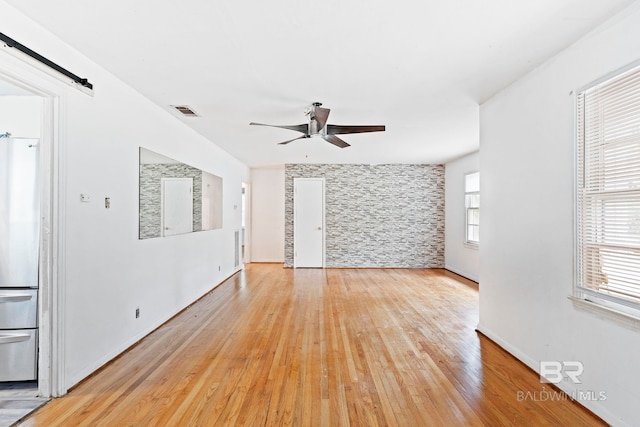 unfurnished room featuring light hardwood / wood-style floors, a barn door, and ceiling fan