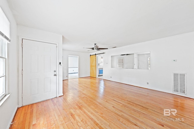 unfurnished living room featuring ceiling fan, a barn door, and light hardwood / wood-style floors