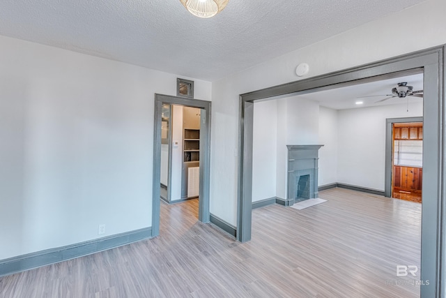 unfurnished living room featuring ceiling fan, light wood-type flooring, a tile fireplace, and a textured ceiling