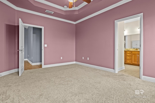 unfurnished bedroom featuring ensuite bathroom, ceiling fan, a raised ceiling, light colored carpet, and ornamental molding