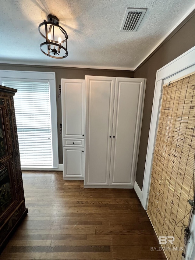 unfurnished bedroom featuring a textured ceiling, dark wood-type flooring, ornamental molding, and a chandelier