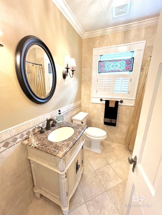 bathroom featuring toilet, tile patterned flooring, crown molding, vanity, and tile walls