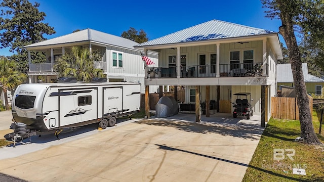 view of front facade featuring concrete driveway, board and batten siding, metal roof, fence, and a carport