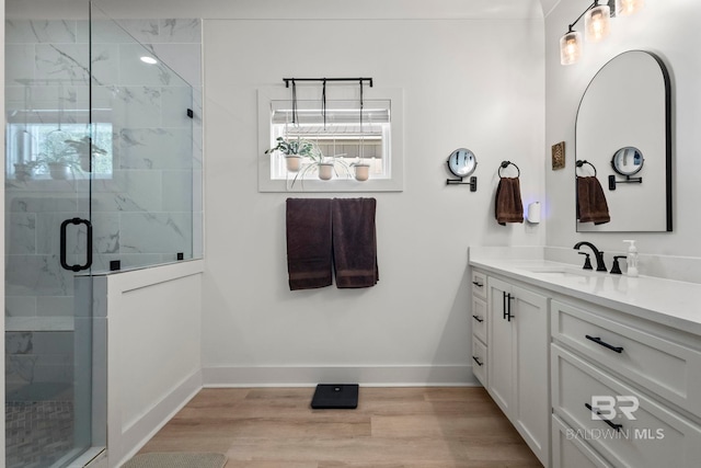 bathroom with wood finished floors, vanity, baseboards, a wealth of natural light, and a stall shower