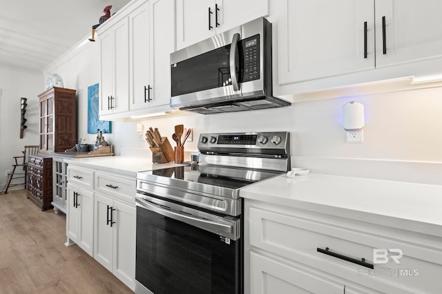 kitchen with stainless steel appliances, white cabinetry, light wood-style floors, light countertops, and ornamental molding