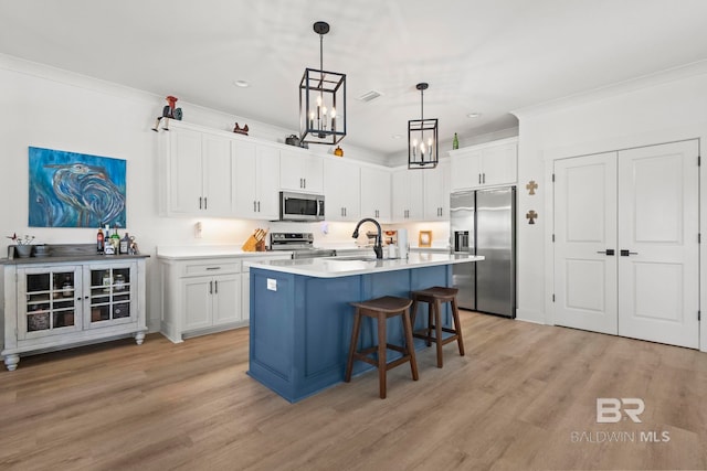 kitchen featuring white cabinets, a breakfast bar area, appliances with stainless steel finishes, crown molding, and a sink