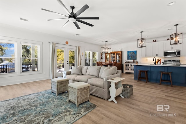 living area with light wood finished floors, french doors, ceiling fan with notable chandelier, and visible vents