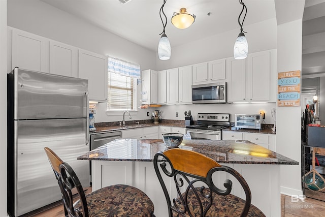 kitchen with dark stone counters, a sink, hanging light fixtures, stainless steel appliances, and white cabinetry