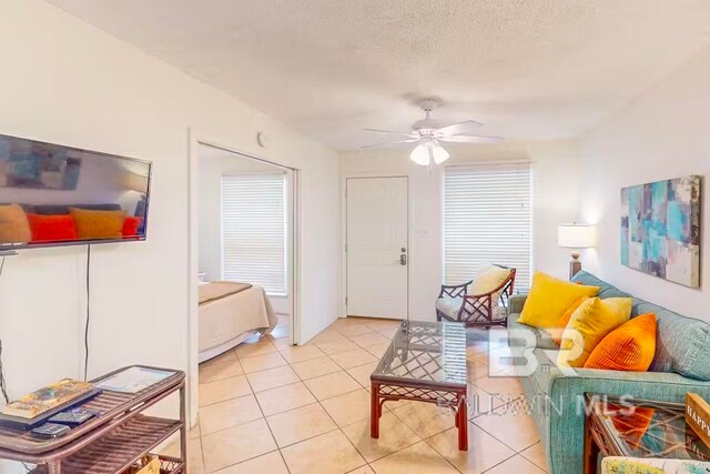 living room with ceiling fan, light tile patterned flooring, and a textured ceiling