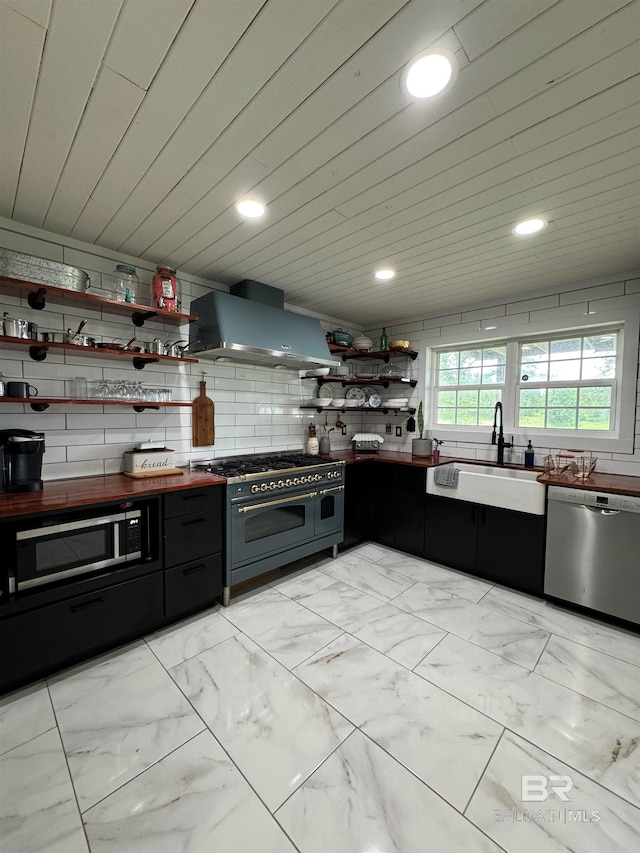 kitchen with light tile patterned floors, appliances with stainless steel finishes, sink, and wall chimney range hood