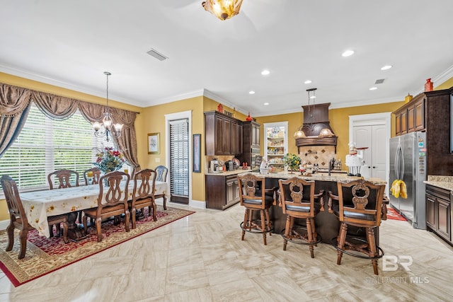 kitchen featuring an island with sink, light tile flooring, premium range hood, backsplash, and stainless steel refrigerator