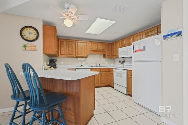 kitchen with white appliances, a skylight, sink, ceiling fan, and light tile patterned flooring