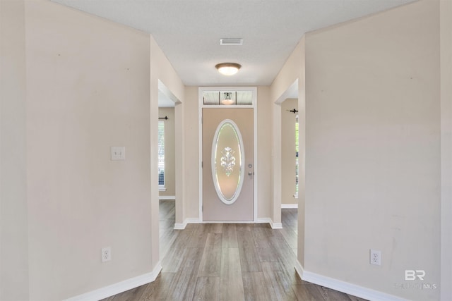 foyer entrance with visible vents, a textured ceiling, baseboards, and wood finished floors