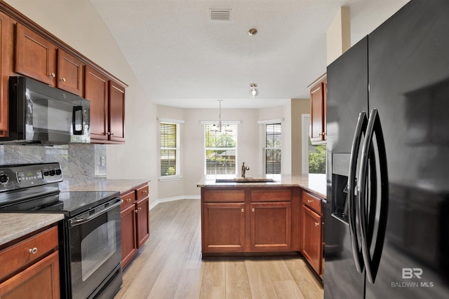 kitchen with light wood-style floors, a peninsula, black appliances, a sink, and decorative backsplash