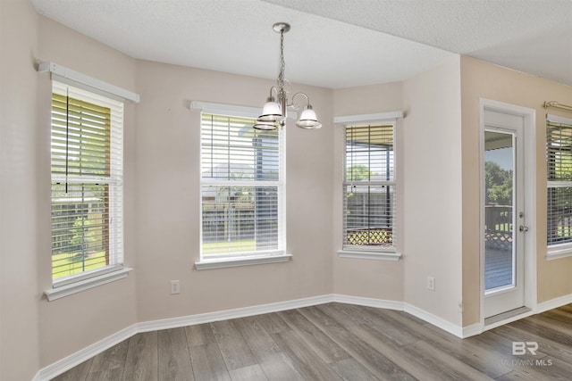 unfurnished dining area with a textured ceiling, baseboards, an inviting chandelier, and wood finished floors