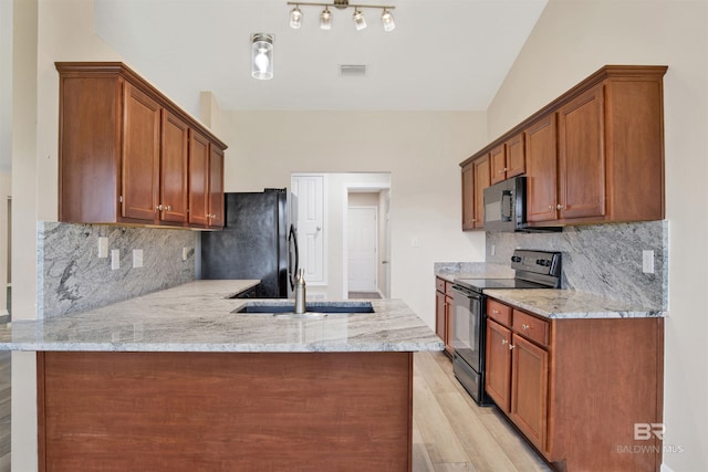 kitchen with light wood-style floors, a peninsula, black appliances, light stone counters, and a sink