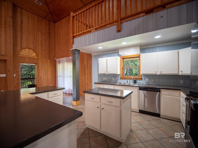 kitchen featuring wood walls, a sink, dark countertops, a towering ceiling, and dishwasher