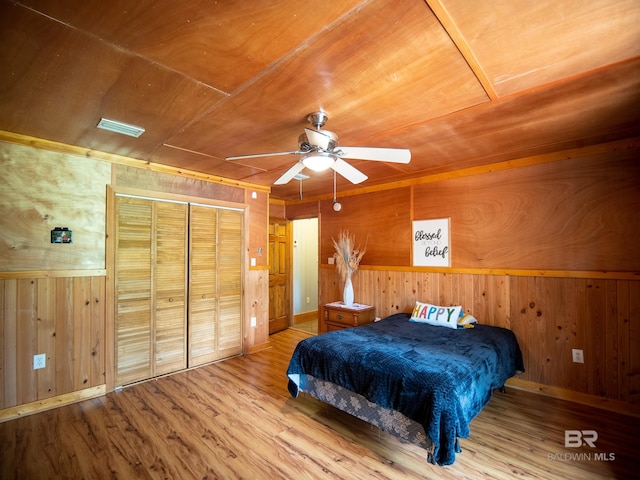 bedroom featuring wood walls, wooden ceiling, a ceiling fan, a closet, and wood finished floors
