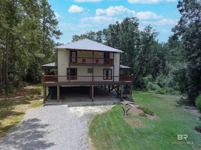 view of front of house with a balcony, metal roof, gravel driveway, a front lawn, and cooling unit