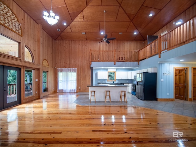 kitchen featuring freestanding refrigerator, a towering ceiling, wood walls, and light wood finished floors