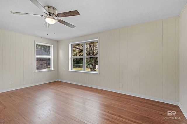 spare room featuring wooden walls, ceiling fan, a textured ceiling, and hardwood / wood-style flooring