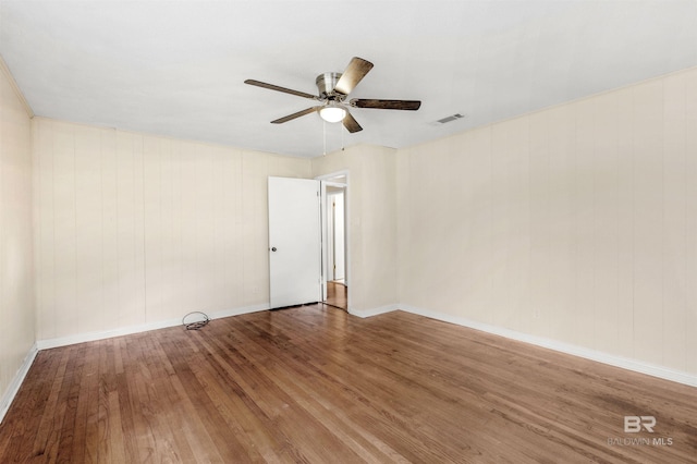 empty room with wood-type flooring, ceiling fan, and wooden walls