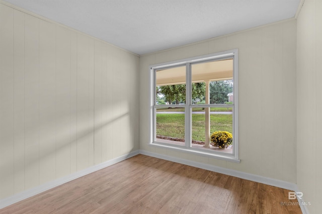 spare room with a textured ceiling, light hardwood / wood-style floors, and wood walls