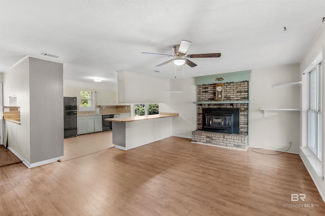 unfurnished living room with a wood stove, light hardwood / wood-style flooring, and ceiling fan