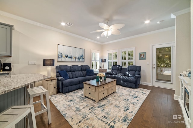 living area featuring dark wood-type flooring, visible vents, baseboards, a ceiling fan, and ornamental molding