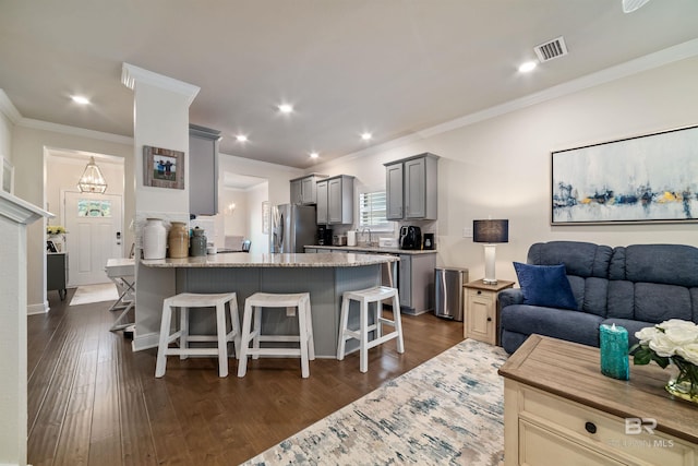 kitchen with dark wood-type flooring, a breakfast bar, gray cabinets, light stone countertops, and stainless steel fridge