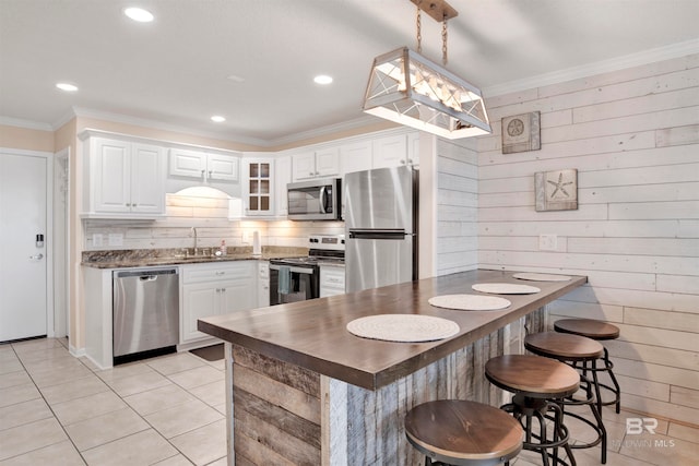 kitchen featuring appliances with stainless steel finishes, white cabinetry, wood walls, and pendant lighting