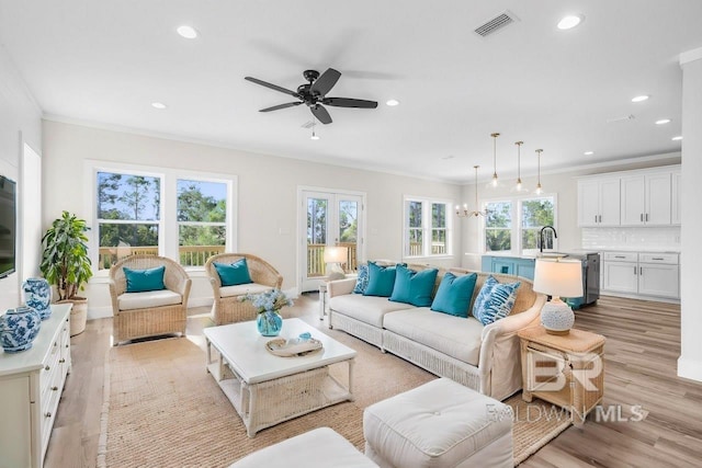 living room featuring ceiling fan with notable chandelier, light wood-type flooring, a healthy amount of sunlight, and crown molding