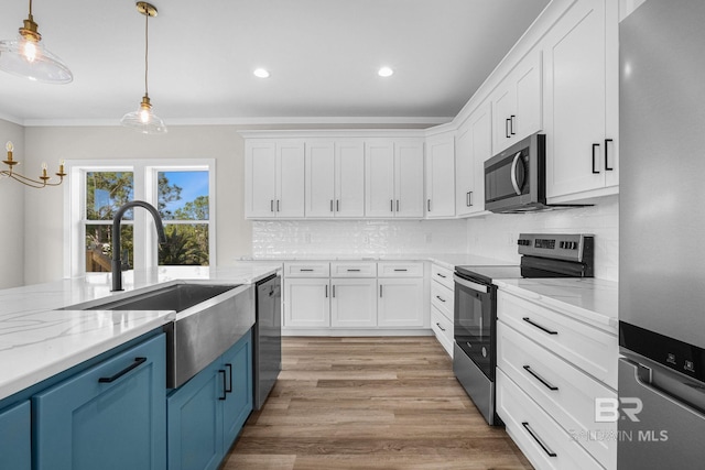 kitchen featuring light wood-type flooring, stainless steel appliances, sink, white cabinetry, and decorative light fixtures