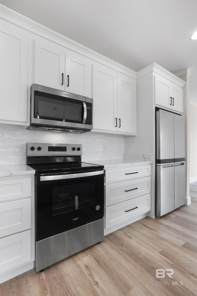 kitchen featuring light wood-type flooring, light stone counters, stainless steel appliances, white cabinets, and backsplash