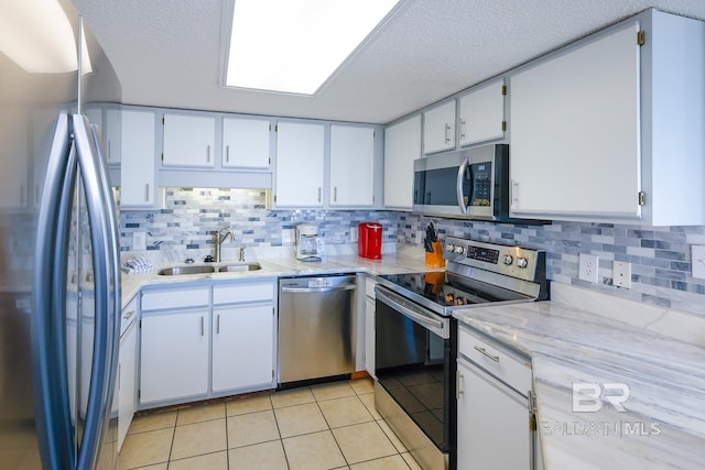 kitchen featuring a sink, backsplash, appliances with stainless steel finishes, light tile patterned flooring, and white cabinets