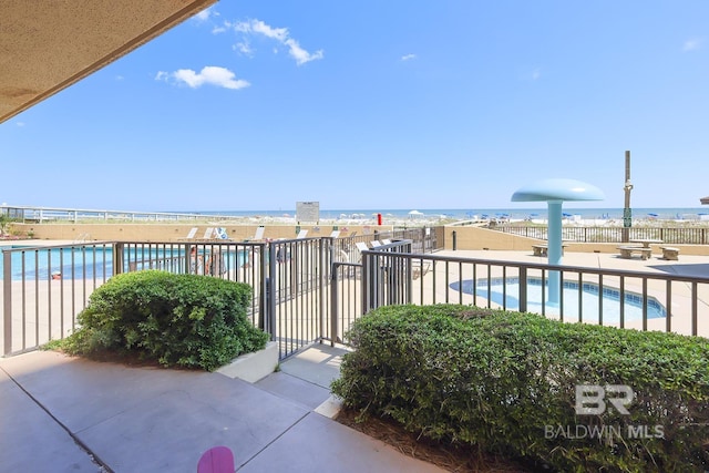 view of patio featuring a community pool, fence, and a water view