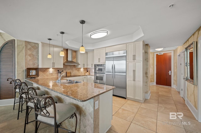 28107 Perdido Beach Blvd Unit D914, Orange Beach, AL 36561 - kitchen with a peninsula, appliances with stainless steel finishes, a breakfast bar area, a tray ceiling, and wall chimney range hood