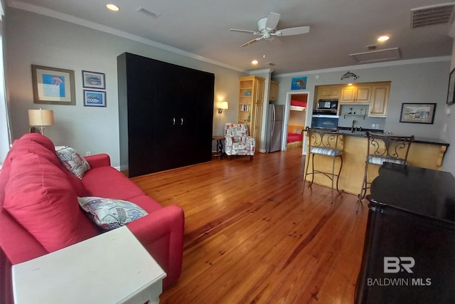 living room featuring light wood-type flooring, attic access, visible vents, and ornamental molding