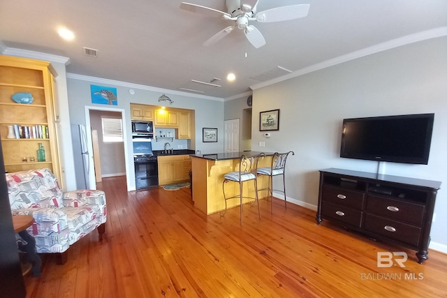 kitchen with a breakfast bar area, visible vents, black appliances, a peninsula, and hardwood / wood-style floors