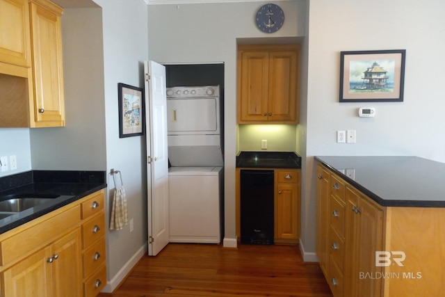 kitchen featuring stacked washer and dryer, baseboards, dark wood-style floors, a peninsula, and a sink